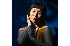 A woman standing in front of a blue background.