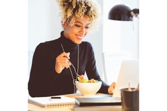 Woman sitting behind her computer eating a healthy lunch.