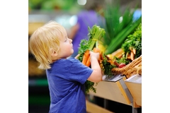 Image Toddler in a supermarket picking up vegetables.