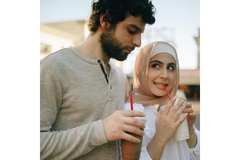 Image A man and a woman drink sweetened beverages in plastic cups through straws while walking in the sun.