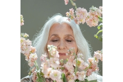 old woman with white hair behind flowers on branches