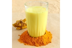 Image Golden turmeric latte in a glass with ground turmeric powder around it.