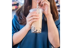 A lady is holding a plastic cup with a straw and drinking bubble tea