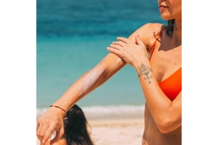 Image A woman rubbing sunscreen into her arm while at the beach.