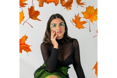 A girl with funky green makeup surrounded by leaves.