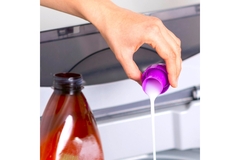 A hand pouring white liquid into a washing machine.