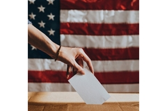 Image A hand putting a ballot into a ballot box.