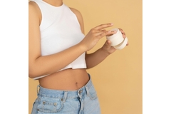Image A woman putting her hand in a jar of skin cream.