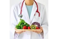 Person in a doctor's coat holding a plate of fruits and vegetables.