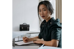 A woman sitting at a desk writing on a piece of paper and looking at the camera.