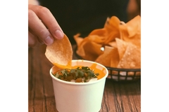 A person dipping a chip into a cup of sauce