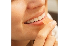 A woman eating an orange colored gummy.