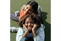 Image a black and a brown girl lay on the grass smiling