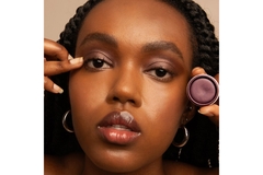 Image A woman holding a pot of eyeshadow and applying it to her eye.