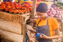 A woman looks at a stone fruit in an open air market.