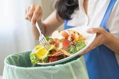 Image a woman's hand throwing food waste in the dustbin.