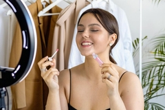 Image A girl holding a lip product smiling to a phone with a ring light.