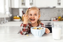 Image a young girl eating breakfast cereal from a white bowl with a spoon.