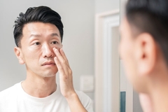 A man looking in the mirror and touching his cheek.