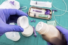 Image Holding medical bottle and closure in hands wearing gloves.