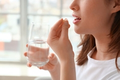 Image A woman taking a pill in a sunlit room.