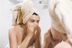 Image A girl looking in the mirror and putting a face scrub on.