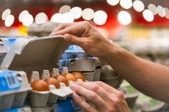 Image a man's hand opening a carton of eggs in the supermarket.
