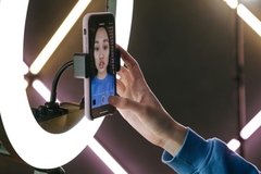 Image A woman clicking the record button on her phone in front of a ring light.