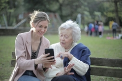 Image young woman shows old women a phone on a bench in the park
