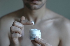 Image A man dipping his finger into eye cream.