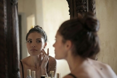 A woman looking in the mirror and touching her face.