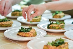 Image a chef's hand plating a dish with coriander.