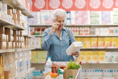 Image an old woman looking at a food package in the supermarket.