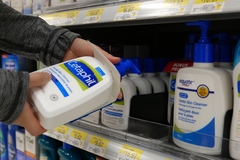 A hand grabbing a bottle of Cetaphil off a shelf.