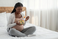 Image Pregnant woman on bed eating bowl of salad