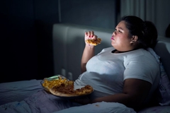 fat woman eating pizza on bed