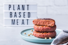 Image three patties stacked in front of sign saying plant based