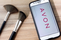 Image Avon's logo on a phone screen next to two makeup brushes