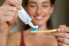 A woman putting toothpaste on a toothbrush.