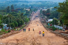 Image A road leading into a lush African village with people walking in brightly colored clothes.