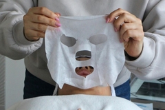 A woman holding up a sheet mask about to put it on someone's face.