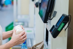 Image A person using self-checkout unit and holding a bag of food