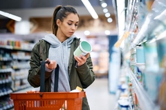 Image Woman carrying grocery basket looks at product label in shop