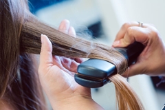 Image Smoke coming from a hair straightener while it is straightening hair.