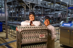 Image two female factory workers standing behind small cartons of milk.