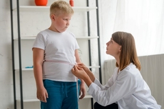 Image An obese chlid get measure by a doctor who stares at him worriedly.