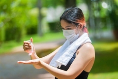 Image A woman wearing a mask outside and putting sunscreen on.