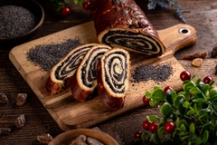 Image Rolled bread full of poppy seeds on cutting board and surrounded by piles of poppy seeds.