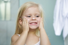 A young kid putting lotion on her face.