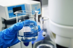 A hand in blue glove holding a beaker